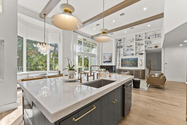 kitchen featuring built in features, sink, a large island with sink, hanging light fixtures, and light stone counters