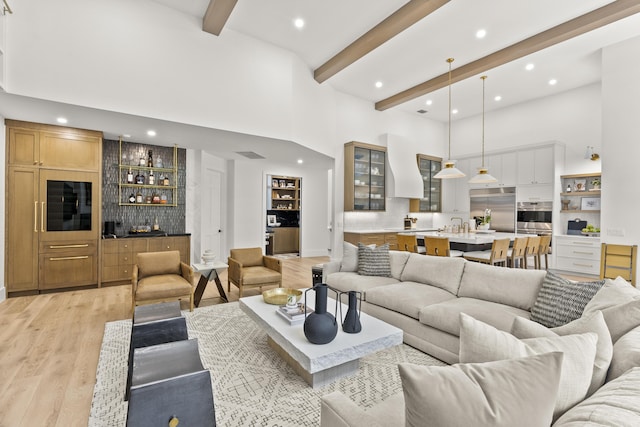 living room featuring a towering ceiling, bar area, beam ceiling, and light hardwood / wood-style flooring