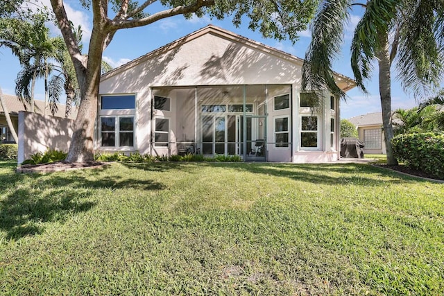 back of property with a sunroom, a lawn, and stucco siding