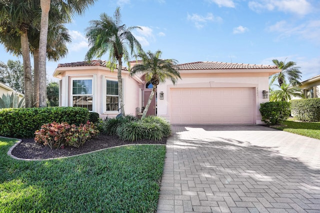 mediterranean / spanish home with a garage, decorative driveway, a tiled roof, and stucco siding