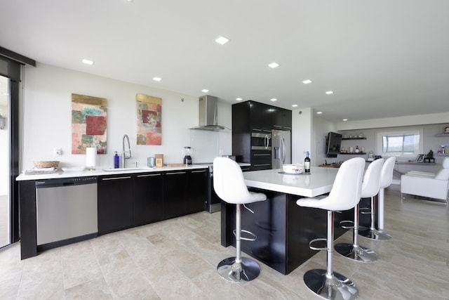 kitchen with kitchen peninsula, wall chimney exhaust hood, a breakfast bar, stainless steel appliances, and sink