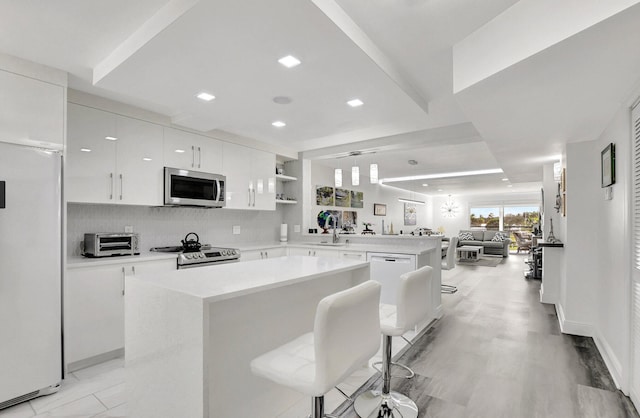 kitchen featuring white cabinetry, stainless steel appliances, light hardwood / wood-style floors, a breakfast bar, and a kitchen island