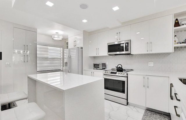 kitchen featuring white cabinets, decorative backsplash, a kitchen island, and appliances with stainless steel finishes