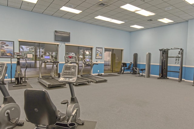 workout area with carpet flooring, a towering ceiling, and a drop ceiling