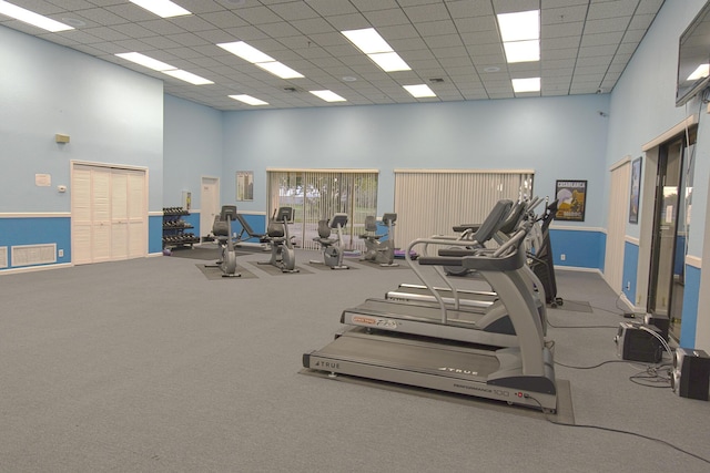 gym featuring carpet flooring, a drop ceiling, and a high ceiling