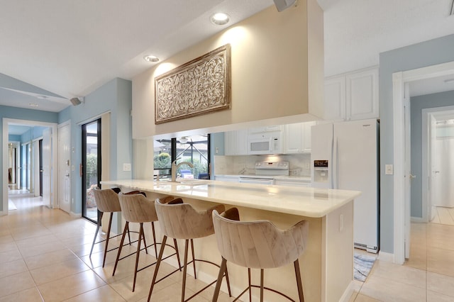 kitchen featuring a breakfast bar, white cabinets, light tile patterned flooring, and white appliances