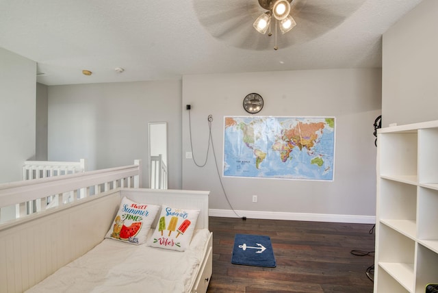 bedroom with dark hardwood / wood-style flooring, a textured ceiling, a nursery area, and ceiling fan