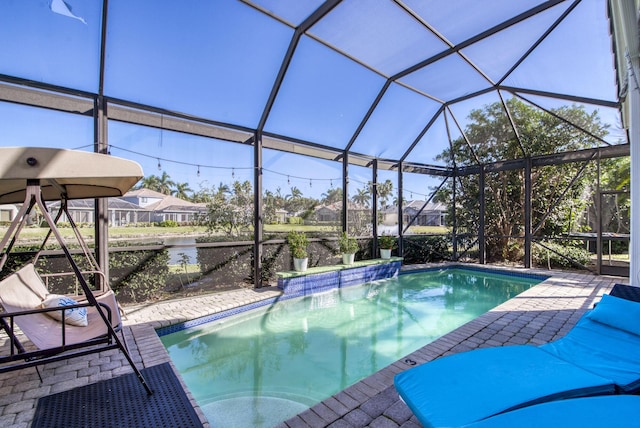 view of pool with a patio area, a water view, pool water feature, and glass enclosure