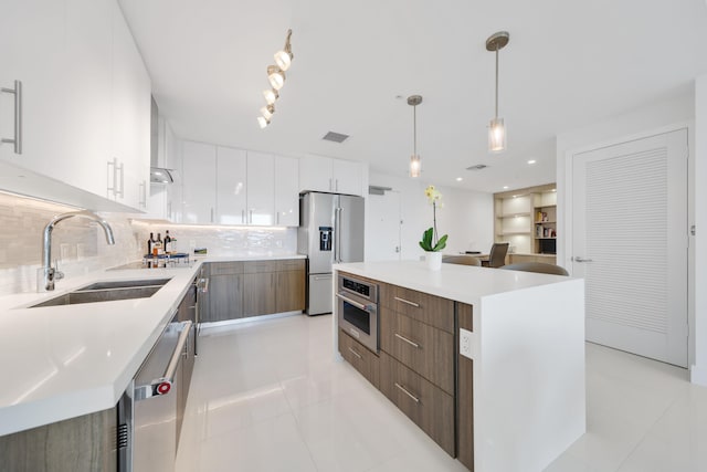 kitchen with pendant lighting, backsplash, white cabinets, wall chimney exhaust hood, and appliances with stainless steel finishes