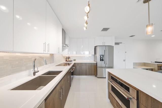 kitchen featuring hanging light fixtures, stainless steel appliances, wall chimney range hood, backsplash, and white cabinets