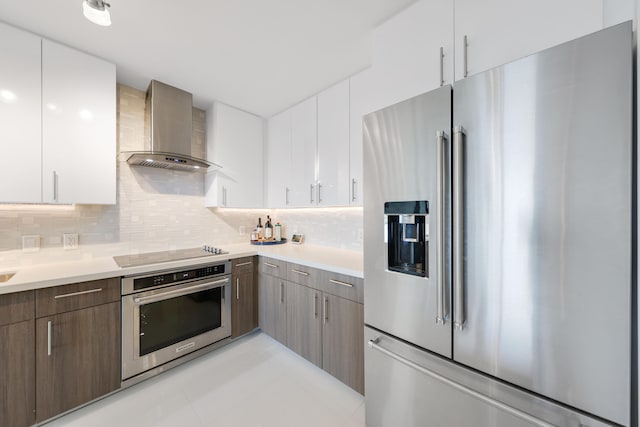 kitchen with white cabinetry, wall chimney exhaust hood, stainless steel appliances, tasteful backsplash, and light tile patterned floors