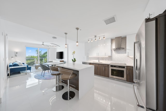 kitchen featuring appliances with stainless steel finishes, backsplash, wall chimney exhaust hood, sink, and a center island