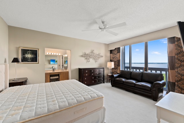 carpeted bedroom with a textured ceiling, ensuite bath, and ceiling fan