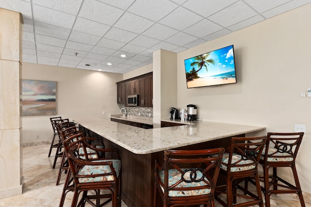 bar with dark brown cabinetry, a paneled ceiling, and decorative backsplash