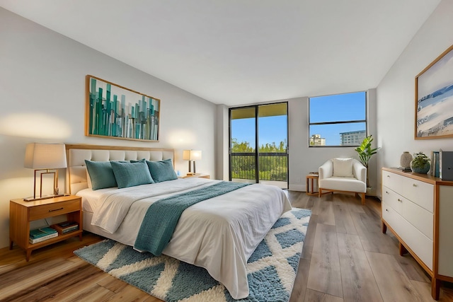 bedroom with access to exterior, light hardwood / wood-style floors, and a wall of windows