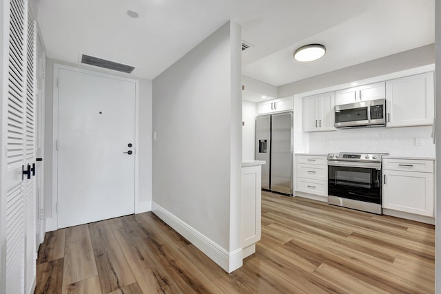 kitchen featuring tasteful backsplash, white cabinetry, light hardwood / wood-style flooring, and appliances with stainless steel finishes