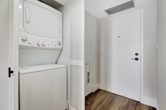 clothes washing area with stacked washer and dryer and dark wood-type flooring