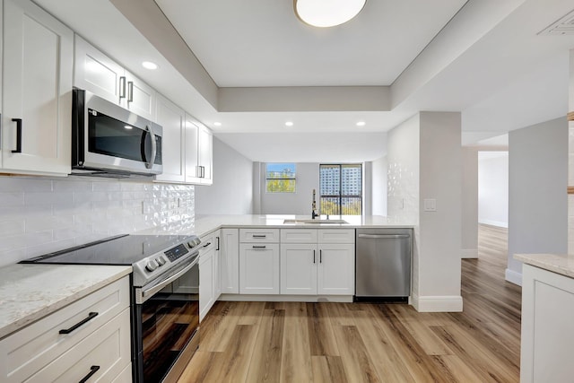 kitchen featuring sink, light hardwood / wood-style flooring, backsplash, white cabinets, and appliances with stainless steel finishes