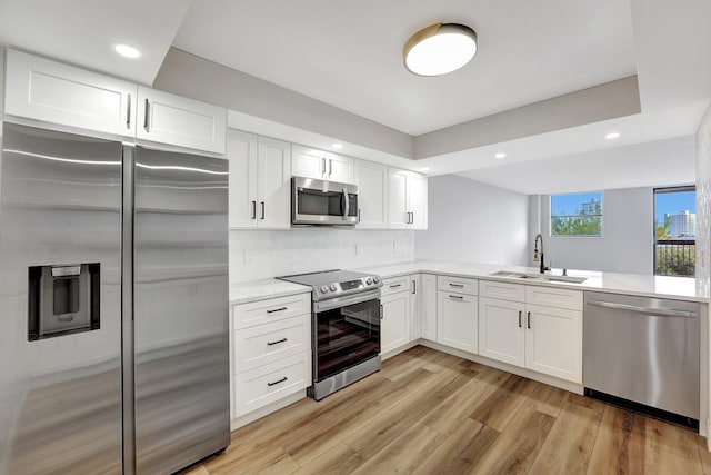 kitchen with backsplash, sink, appliances with stainless steel finishes, light hardwood / wood-style floors, and white cabinetry