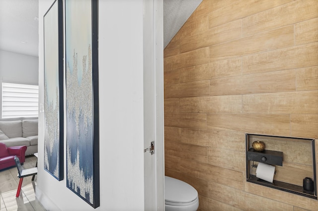 bathroom with a textured ceiling, toilet, and wooden walls