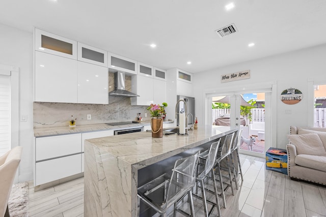 kitchen featuring white cabinetry, a breakfast bar, wall chimney range hood, and a center island with sink