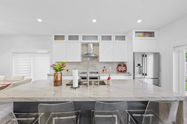 kitchen featuring white cabinetry, wall chimney exhaust hood, a kitchen bar, decorative backsplash, and high end fridge