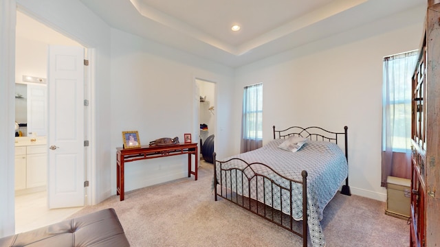 bedroom with a raised ceiling, light carpet, and ensuite bath