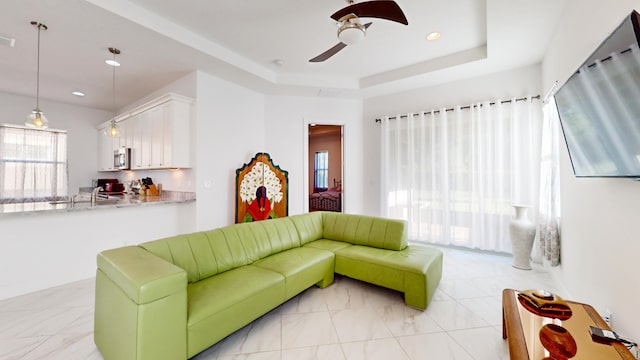 living room with a raised ceiling and ceiling fan