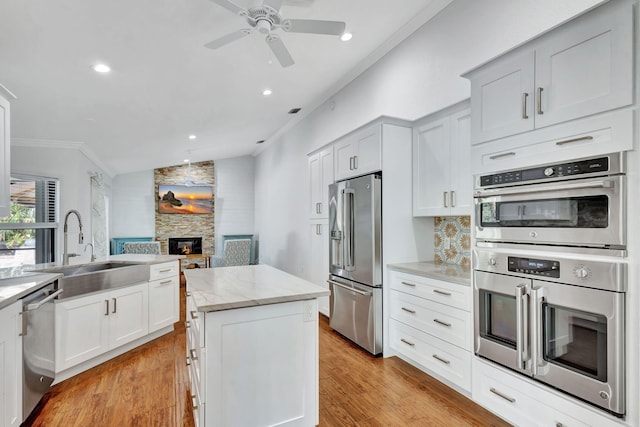 kitchen featuring a stone fireplace, light wood-type flooring, ornamental molding, appliances with stainless steel finishes, and a kitchen island