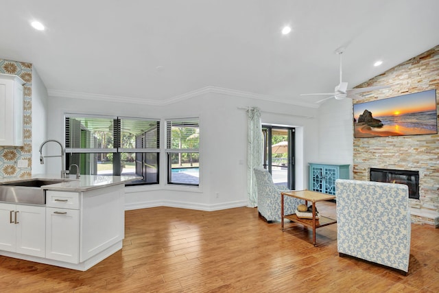 kitchen with a stone fireplace, white cabinetry, sink, and light hardwood / wood-style floors