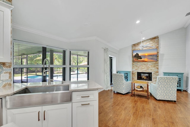 kitchen featuring lofted ceiling, sink, light wood-type flooring, a fireplace, and white cabinetry