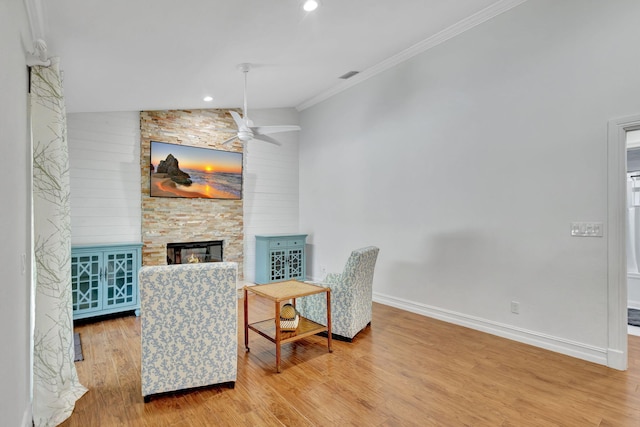 living area with ceiling fan, crown molding, hardwood / wood-style floors, lofted ceiling, and a fireplace