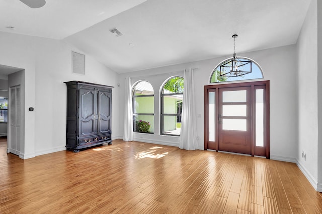 foyer entrance featuring light wood-type flooring, high vaulted ceiling, and an inviting chandelier