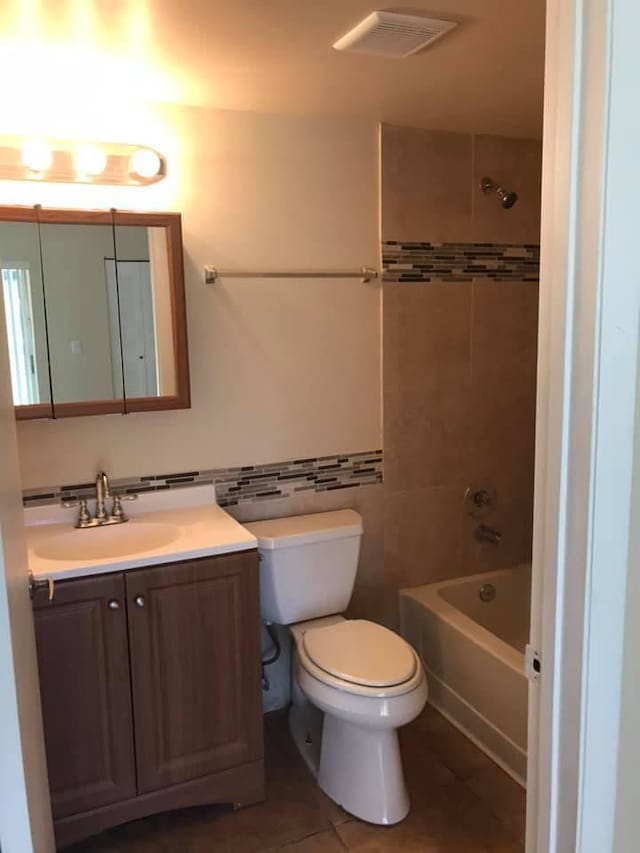 full bathroom with tile patterned floors, vanity, tiled shower / bath, and toilet