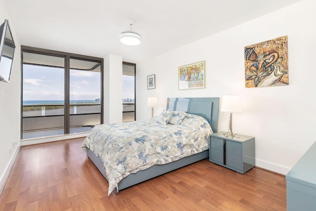 bedroom featuring access to exterior, hardwood / wood-style floors, and a wall of windows