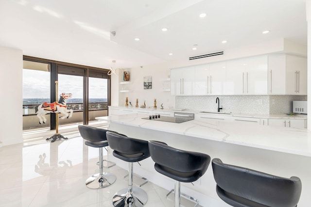 kitchen with black electric stovetop, sink, light stone counters, a kitchen bar, and white cabinetry