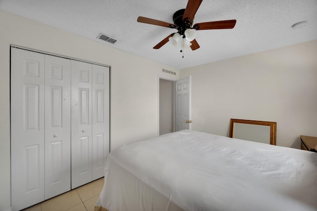 tiled bedroom with ceiling fan, a textured ceiling, and a closet