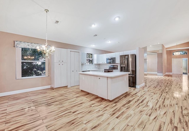 kitchen with white cabinets, light hardwood / wood-style floors, appliances with stainless steel finishes, decorative light fixtures, and a kitchen island