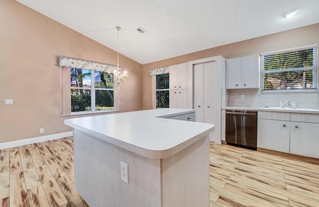 kitchen with dishwasher, hanging light fixtures, plenty of natural light, vaulted ceiling, and white cabinets