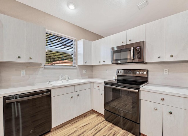 kitchen with backsplash, sink, light hardwood / wood-style floors, white cabinetry, and stainless steel appliances