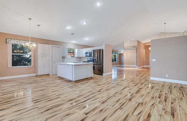 unfurnished living room with ceiling fan with notable chandelier, lofted ceiling, and light hardwood / wood-style flooring