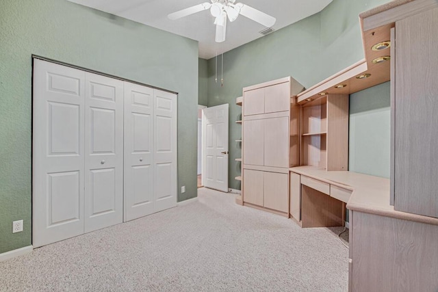 unfurnished office with built in desk, light colored carpet, and ceiling fan