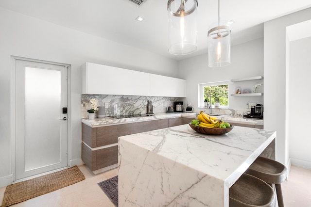 kitchen with a center island, backsplash, light stone countertops, decorative light fixtures, and white cabinetry