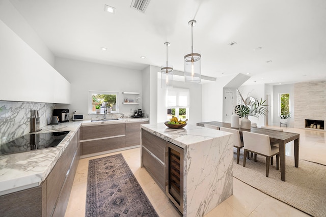 kitchen with light stone countertops, beverage cooler, decorative light fixtures, black electric cooktop, and a kitchen island