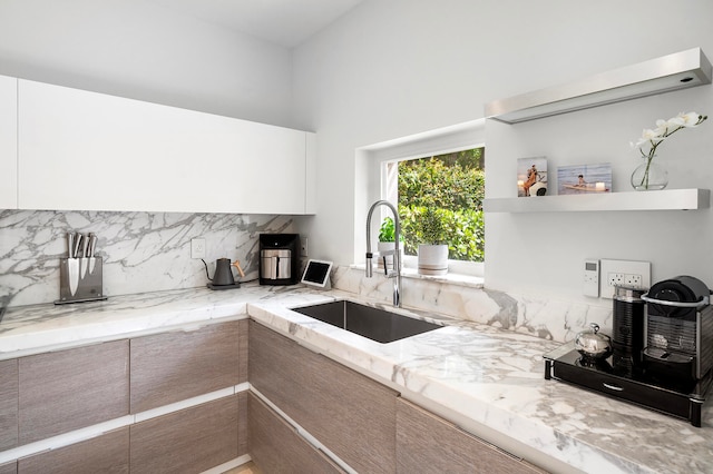 kitchen with tasteful backsplash, light stone countertops, sink, and white cabinets