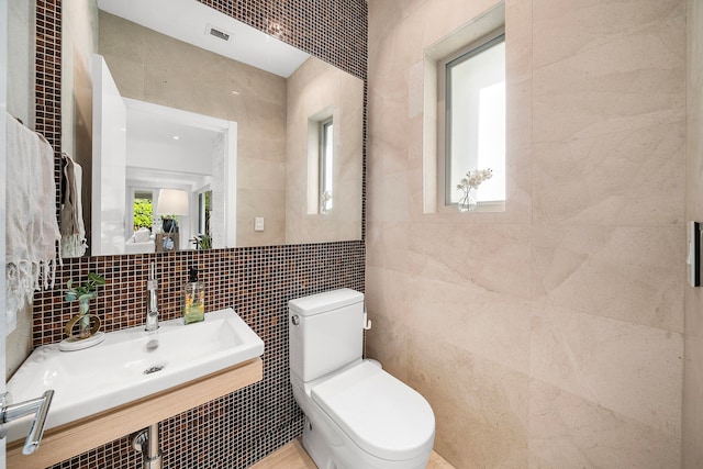 bathroom with toilet, tile walls, and sink