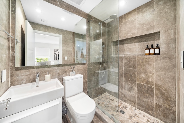 bathroom with vanity, decorative backsplash, toilet, tiled shower, and tile walls