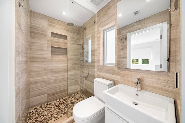 bathroom with vanity, toilet, tile walls, and a tile shower