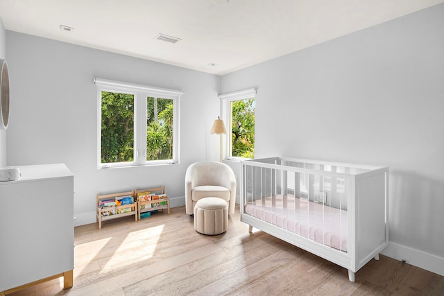 bedroom with light wood-type flooring and a nursery area