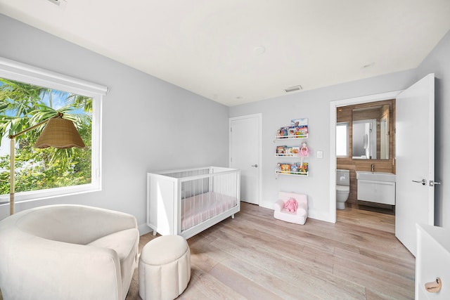 bedroom featuring sink, a crib, light hardwood / wood-style flooring, and ensuite bath